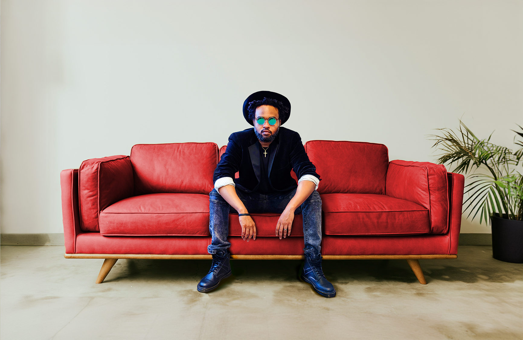 a man wearing a cross and hat sat down in the middle of a large red sofa
