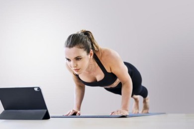 A lady doing push ups in front of a laptop