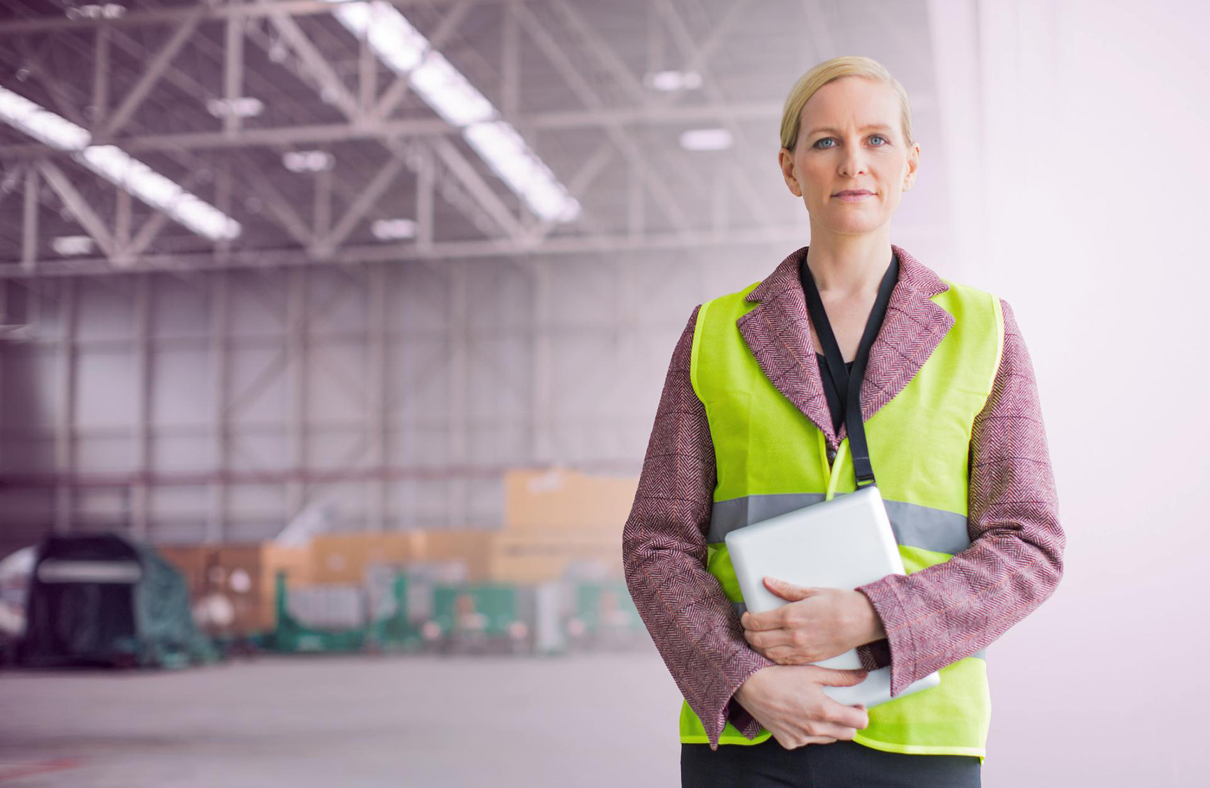a serious woman holding onto a laptop in the middle of a warehouse