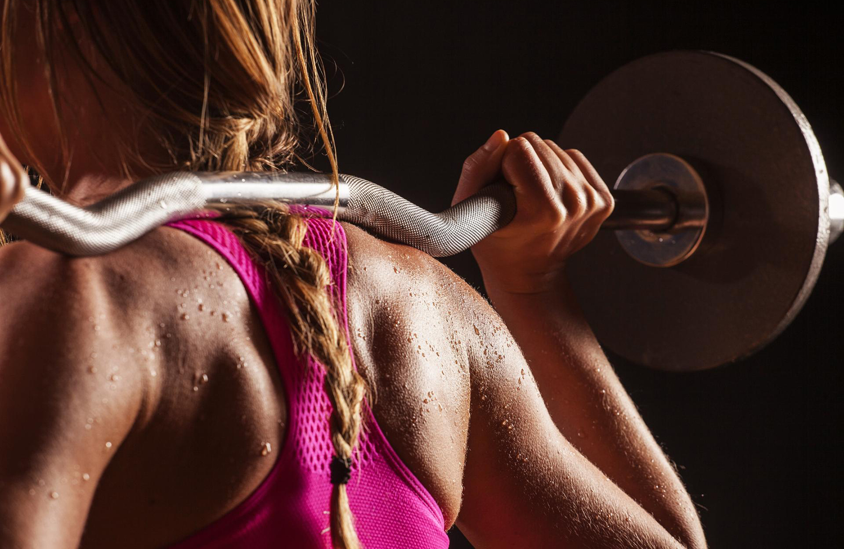 an athletic womans back as she squats with weights