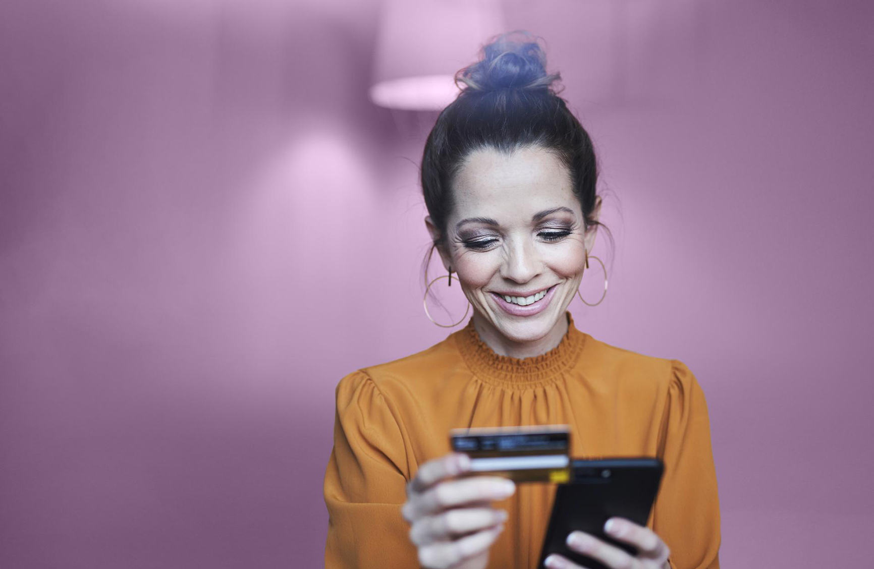 a smiling woman holding a phone whilst reading off of a credit card