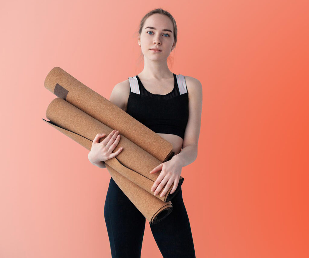Young woman in sports gear holding a pile of yoga mats